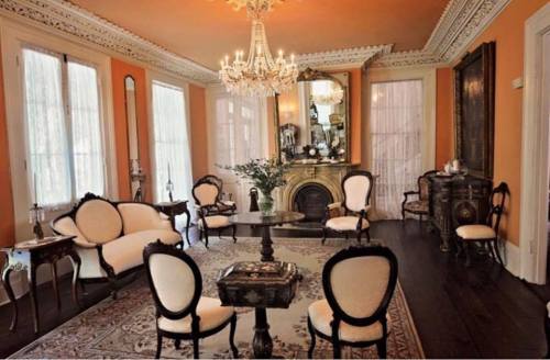 Elegant living room with orange walls, a chandelier, vintage furniture, and a decorative mirror above a fireplace.