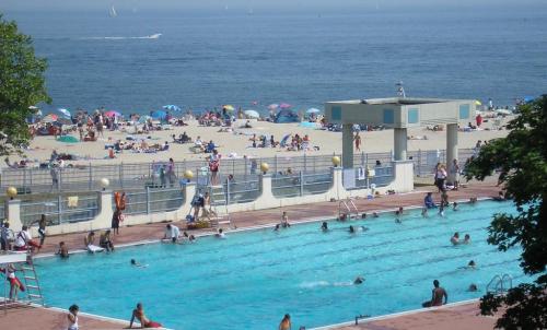 A busy beach scene with a swimming pool in the foreground and people relaxing on the sand in the background.