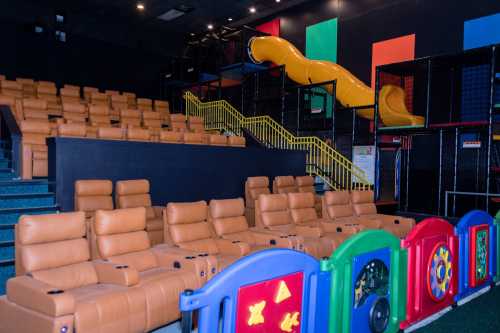 A colorful indoor play area with seating and a yellow slide, featuring plush chairs and interactive play panels.