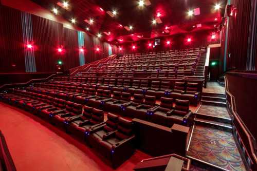 A spacious movie theater with red lighting and plush reclining seats, arranged in a tiered layout.