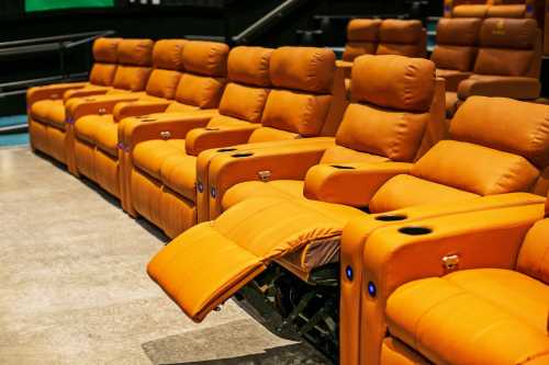 A row of orange reclining theater seats with cup holders, arranged in a modern cinema setting.