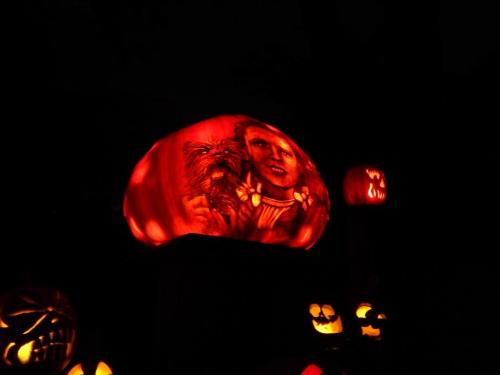 A glowing carved pumpkin with a detailed face design, surrounded by other jack-o'-lanterns in a dark setting.