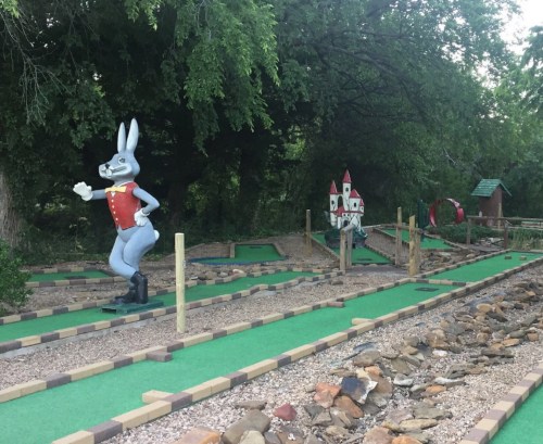 A whimsical mini-golf course featuring a cartoon rabbit and a castle, surrounded by greenery and rocky pathways.