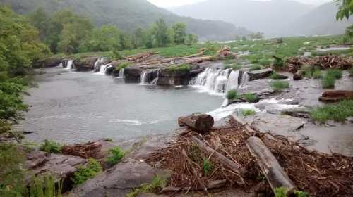 A serene landscape featuring small waterfalls cascading over rocks, surrounded by greenery and misty mountains in the background.