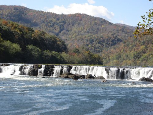 A scenic view of a waterfall cascading over rocks, surrounded by lush green hills and a clear blue sky.