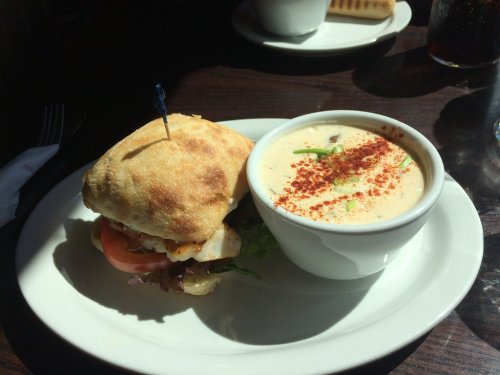 A sandwich with grilled chicken, lettuce, and tomato, served with a bowl of creamy soup garnished with spices.