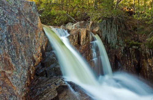 A serene waterfall cascading over rocky terrain, surrounded by lush green trees and natural scenery.