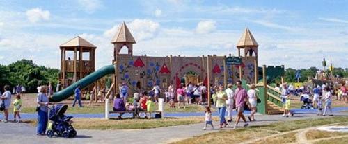 A busy playground with a large play structure, families, and children enjoying a sunny day outdoors.