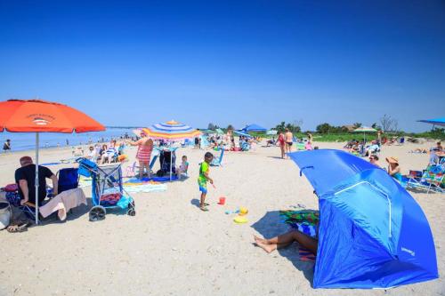 A sunny beach scene with people relaxing under umbrellas, children playing, and colorful beach gear scattered on the sand.