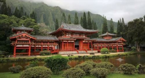 A traditional Japanese-style building with red accents, surrounded by lush greenery and a tranquil pond.
