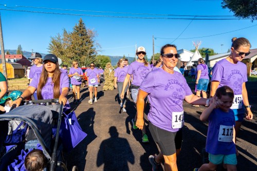 A group of participants in purple shirts walking in a community event, some pushing strollers and others holding hands.