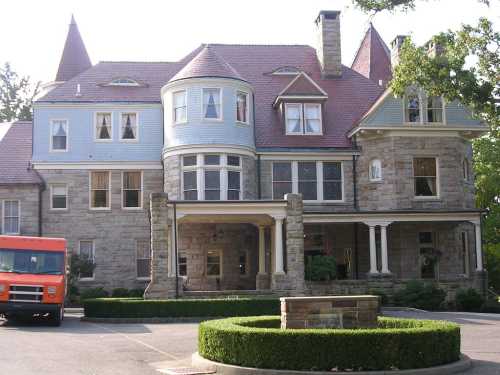 A large, historic stone mansion with a blue and gray exterior, featuring multiple gables and a circular tower.