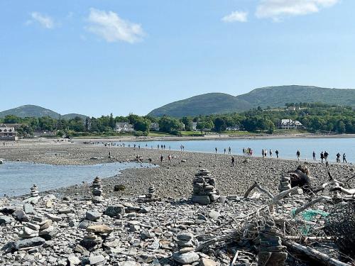 A scenic beach with people walking along the shore, rocky terrain, and hills in the background under a clear blue sky.
