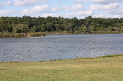 A serene lake surrounded by lush greenery and trees under a partly cloudy sky.