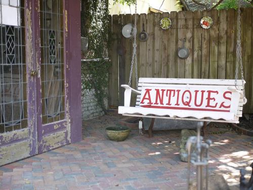 A white swing with "ANTIQUE" painted in red, set against a rustic wooden fence and a brick patio.