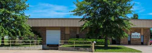 A brick building with a metal roof, surrounded by trees, featuring a sign that reads "Books" near a loading dock.