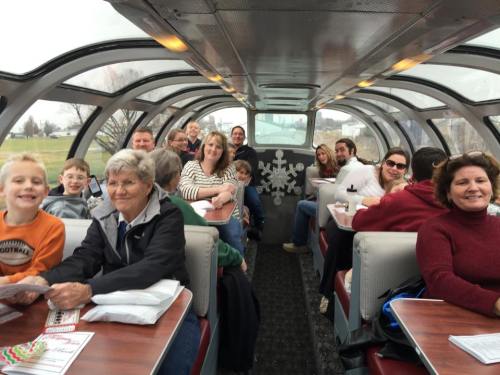 A group of people seated in a train car with large windows, smiling and enjoying their time together.