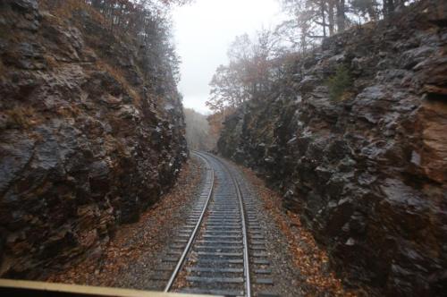 A winding railway track surrounded by rocky cliffs and autumn foliage on a foggy day.