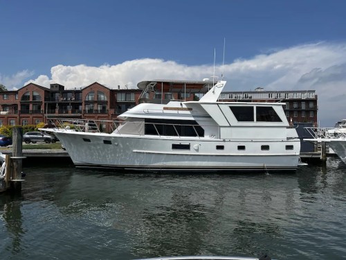 A white yacht docked in a marina with buildings in the background under a clear blue sky.