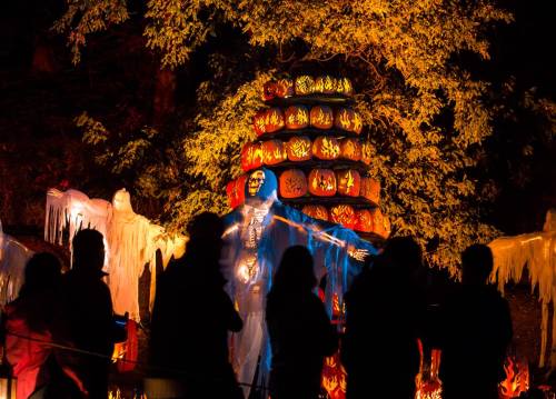 A colorful Halloween display featuring a skeletal figure surrounded by glowing pumpkins and ghostly figures, with onlookers.