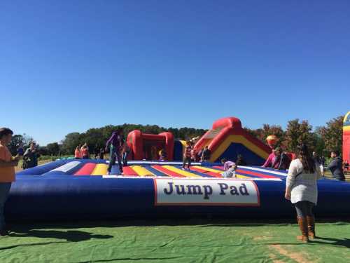 A colorful inflatable jump pad with children playing, surrounded by adults on a sunny day.