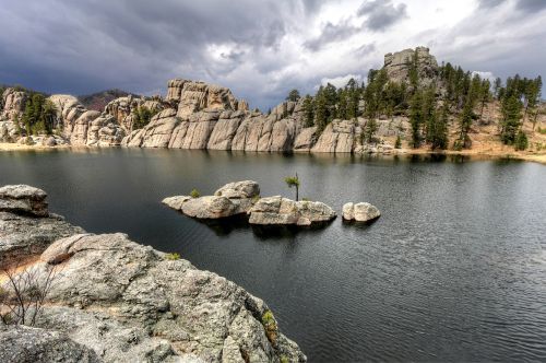 A serene lake surrounded by rocky formations and pine trees under a cloudy sky.