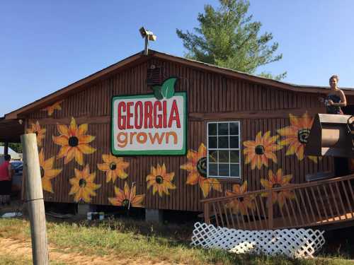 A wooden building with a colorful "Georgia Grown" sign and sunflower mural, surrounded by greenery.