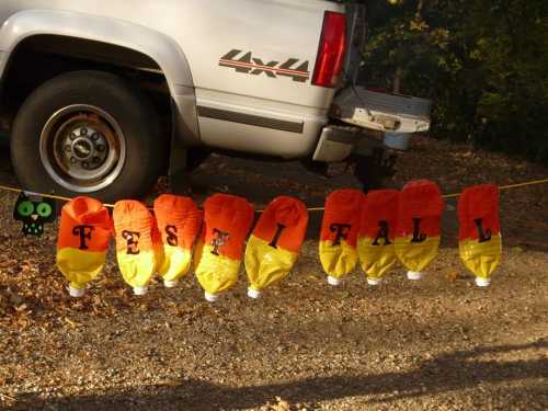 A festive fall decoration made of orange and yellow lanterns spelling "FESTIFALL" hanging near a truck.