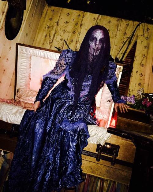 A ghostly figure in a dark, tattered dress emerges from an ornate coffin, surrounded by a dimly lit, eerie setting.