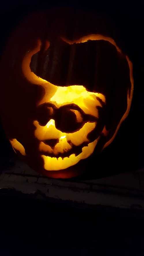 A carved pumpkin glowing with a detailed face design, featuring a playful expression and wavy hair.