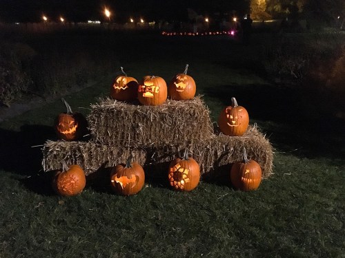 A display of carved pumpkins on a haystack at night, featuring various spooky designs and glowing lights.
