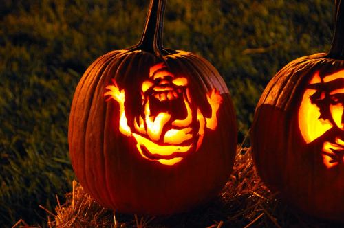 Two carved pumpkins glow in the dark, one featuring a whimsical monster design, set against a grassy background.