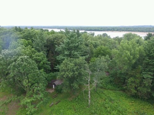 Aerial view of a lush green forest with a small cabin and a river in the background.