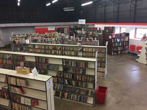 A spacious library with tall bookshelves filled with books, organized in rows, and a few red chairs visible.