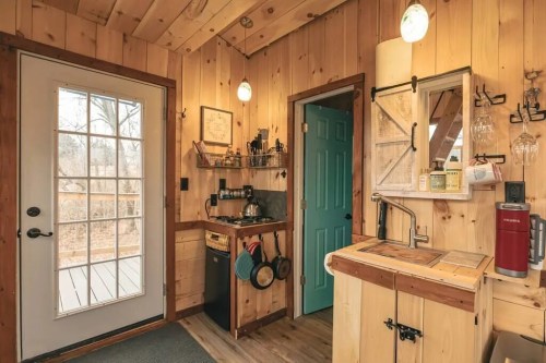 Cozy wooden interior of a small kitchen with a door, sink, and shelves, featuring warm lighting and rustic decor.