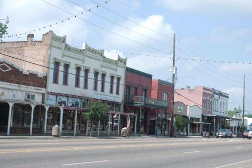 Historic buildings line a street, featuring a mix of architectural styles and storefronts under a blue sky.