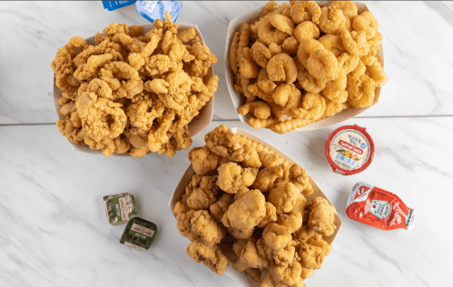 Three large bowls filled with crispy fried chicken pieces, accompanied by dipping sauces on a marble surface.