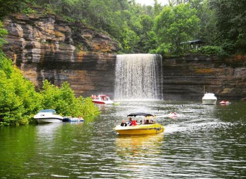 A scenic view of a waterfall surrounded by lush greenery, with boats on the water enjoying the serene landscape.