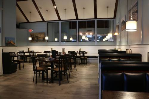 Interior of a restaurant featuring wooden beams, tables, and booths, with soft lighting and a calm atmosphere.