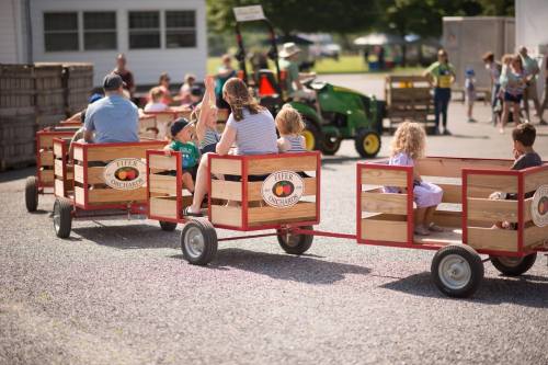 A group of children and adults ride on a wooden wagon pulled by a tractor at a farm event.