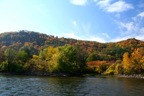 A serene river scene with vibrant autumn foliage on rolling hills under a clear blue sky.
