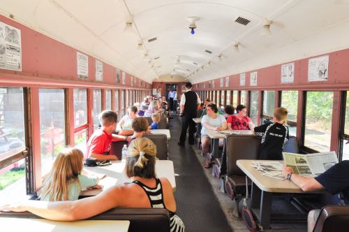 Interior of a bus converted into a classroom, with children and adults seated at tables, engaged in activities.