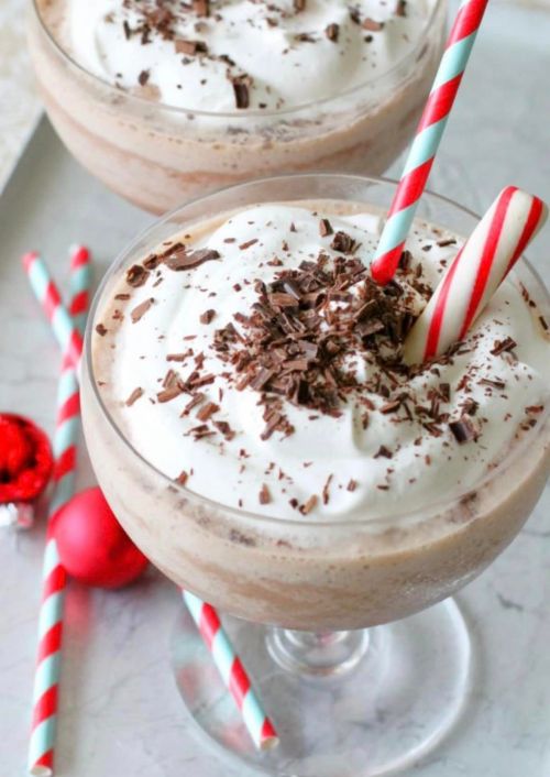 Two festive desserts in glass cups topped with whipped cream, chocolate shavings, and a candy cane, with striped straws.