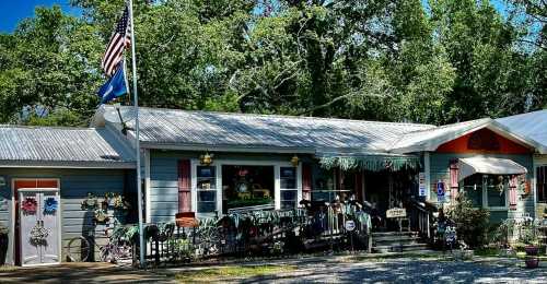 A charming storefront with a porch, surrounded by trees, featuring decorative items and an American flag.