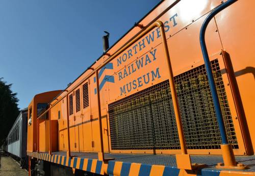 Orange train car with "Northwest Railway Museum" signage, set against a clear blue sky.