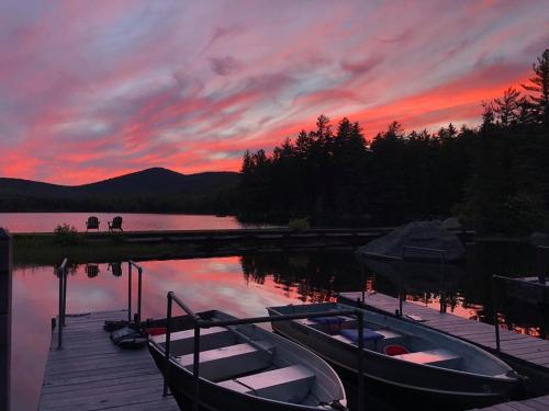 A serene lake at sunset, with vibrant pink and orange skies reflecting on the water, surrounded by trees and mountains.