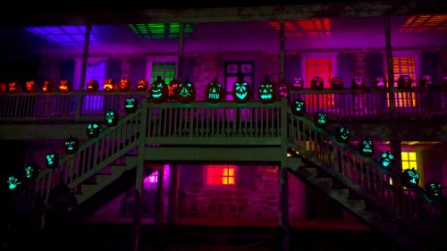 A spooky display of glowing jack-o'-lanterns on a staircase, with colorful lights illuminating a historic building.