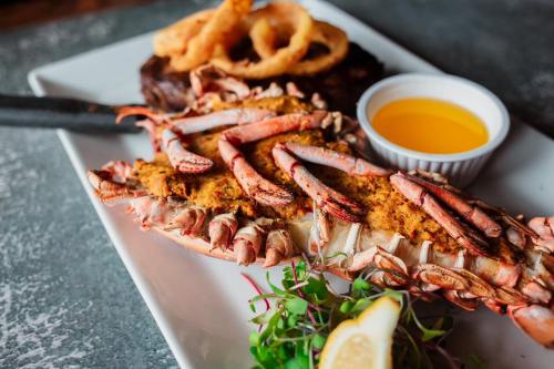A plate featuring grilled lobster with seasoning, a side of steak, onion rings, and a lemon wedge.