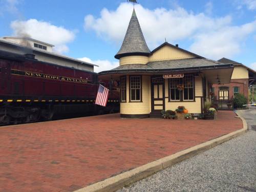 A charming train station with a turret, featuring an American flag and a vintage train in the background.
