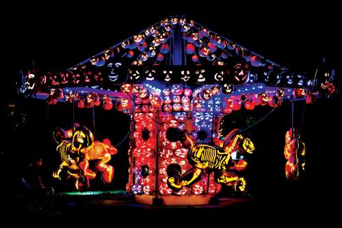 A brightly lit carousel featuring skeletons and pumpkin faces, set against a dark night sky.